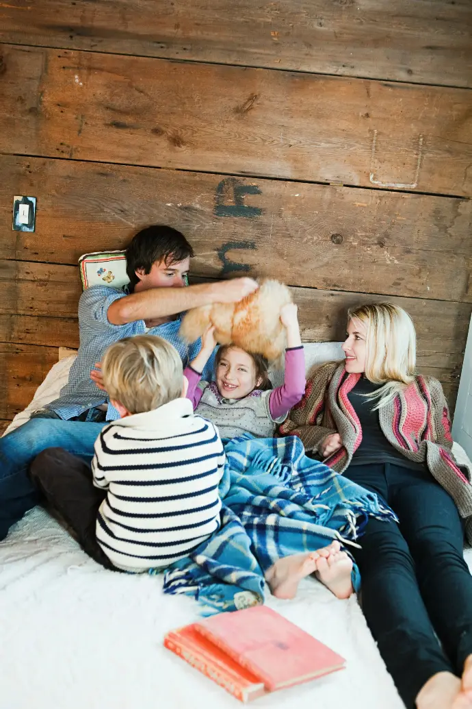 Familia compuesta por un padre, una madre y dos hijos jugando en la cama